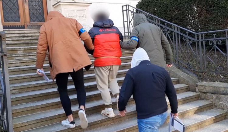 Kriminalisté eskortují obviněného muže k soudu, kde se rozhodovalo o jeho vzetí do vazby