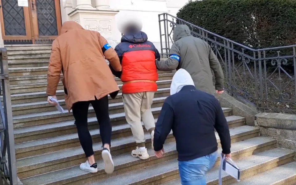 Kriminalisté eskortují obviněného muže k soudu, kde se rozhodovalo o jeho vzetí do vazby